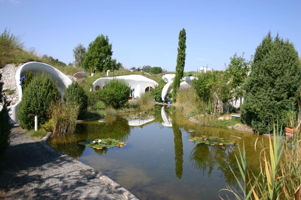 Auch in der Schweiz wurden verschiedene Earthships realisiert; hier ein kleiner Teich, umgeben von weißen blasenförmigen Earth Houses