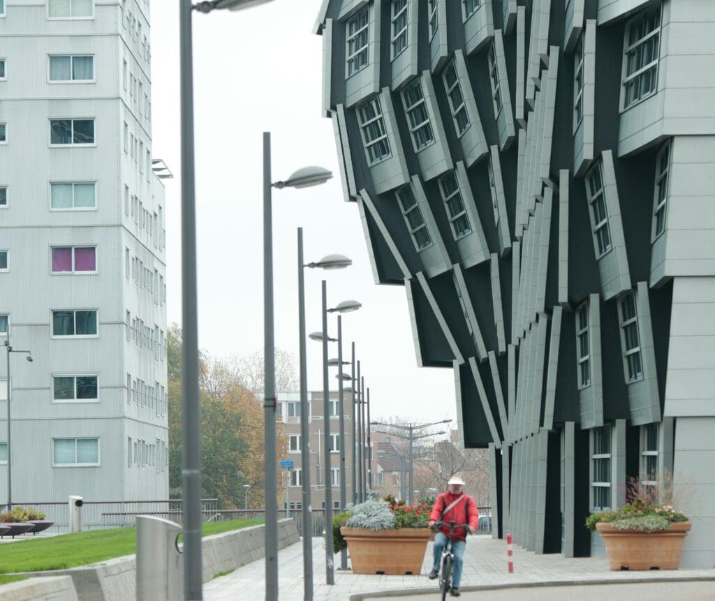 Radfahrer vor dem Gebäude "The Wave" in Almere Stad Dieses Wohngebäude ist bekannt für seine markante, wellenförmige Fassade und die hervorstehenden Fenster, die ein dynamisches, wellenförmiges Aussehen erzeugen.