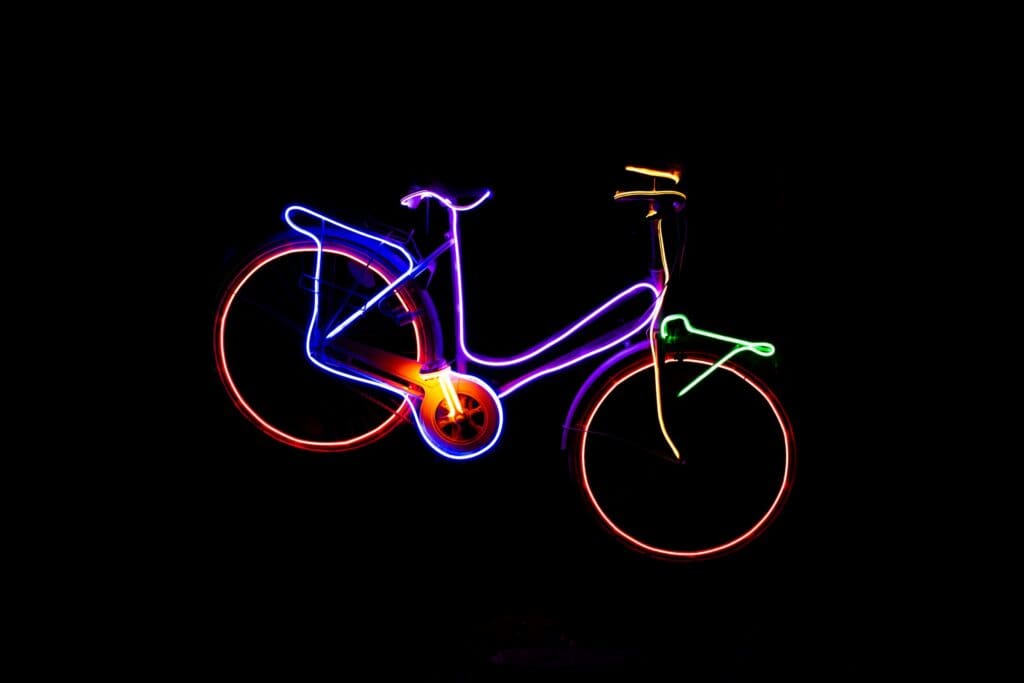 A bicycle made out of green, yellow, purple and orange neon tube, on a black background; neon tubes use a cold plasma to produce light 