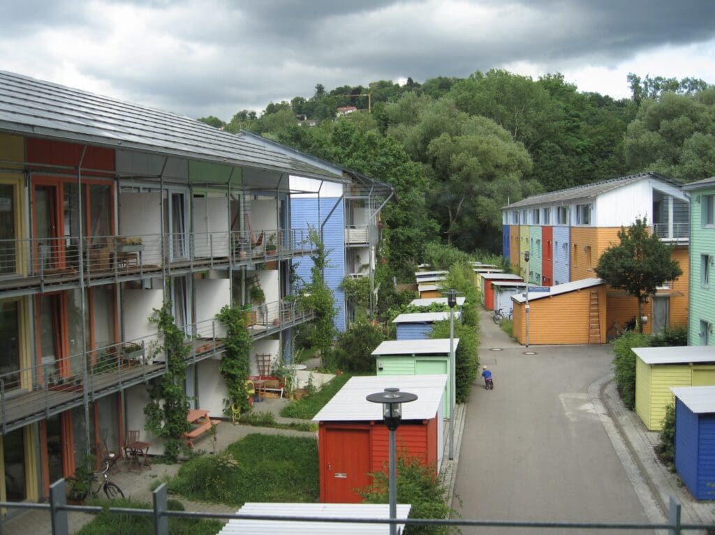 Das Freiburger Öko-Viertel Vauban besteht aus bunten Häuserzeilen, die von Grün umgeben sind. Auf der verkehrsberuhigten Spielstraße'fährt ein kleines Kind auf seinem Mini-Fahrrad. 
