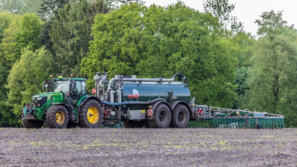 Gülle wird von einem Traktor mit Anhänger auf einem braunen Feld ausgebracht