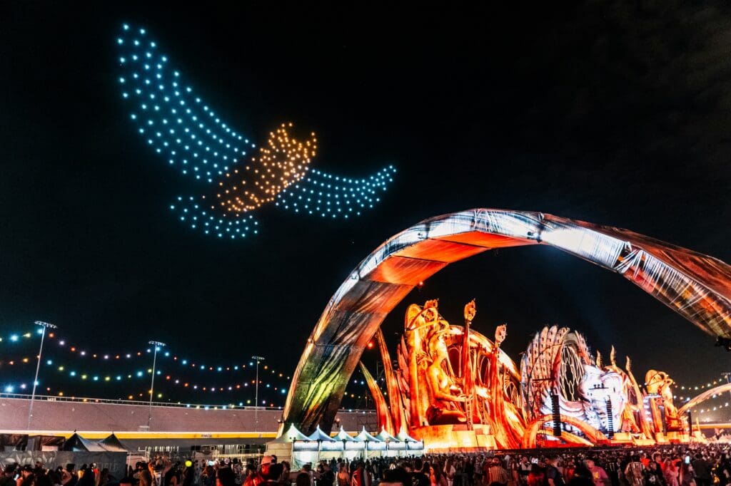 Colorful drone light show with a golden and turquoise owl made out of illuminated drones against the night sky